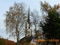 Věž kostela mezi podzimními korunami stromů